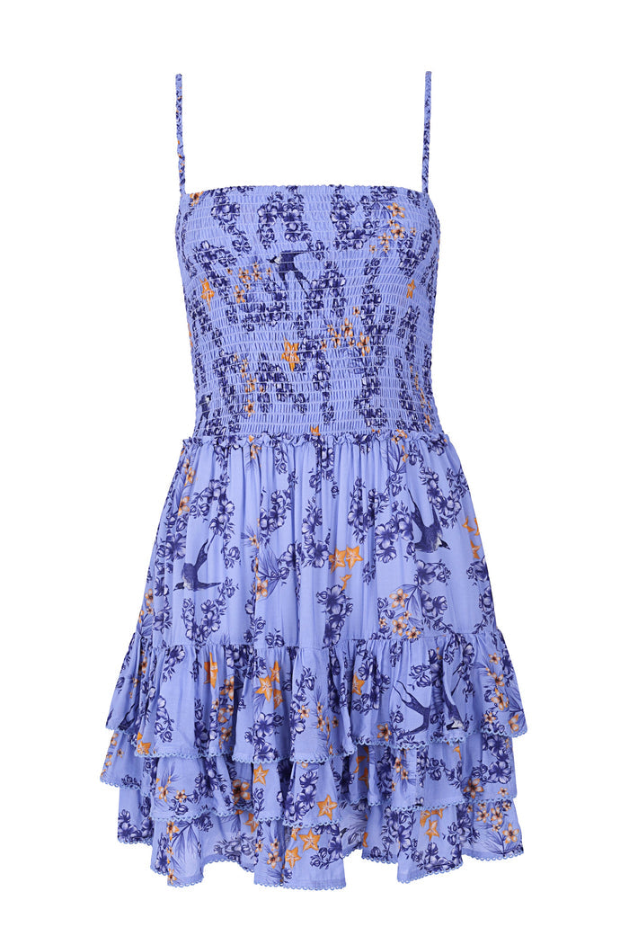 Periwinkle mini dress with smocked bodice, adjustable straps, tiered ruffle skirt, and navy and orange pattern detail print throughout
