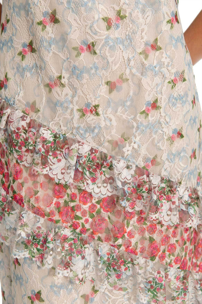 White lace maxi dress with blue pattern detail embroidery and pink rose print border at ruffle hem