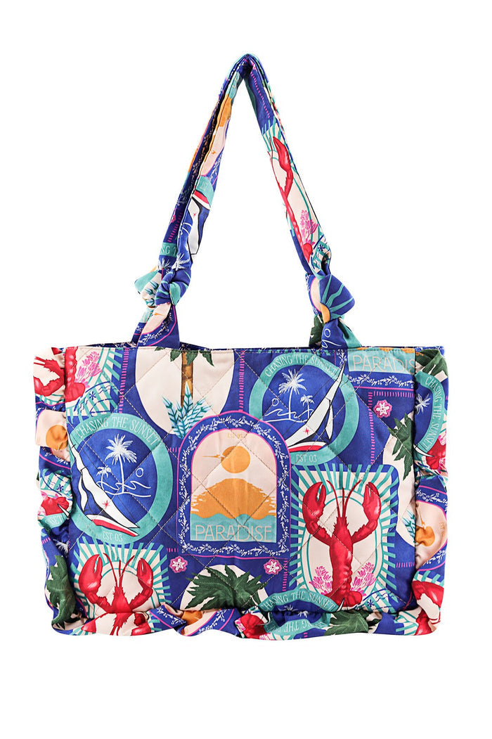 Quilted tote bag with multicolor tropical print featuring circular emblems of palm trees, lobsters, and sunset graphics on blue and cream background…