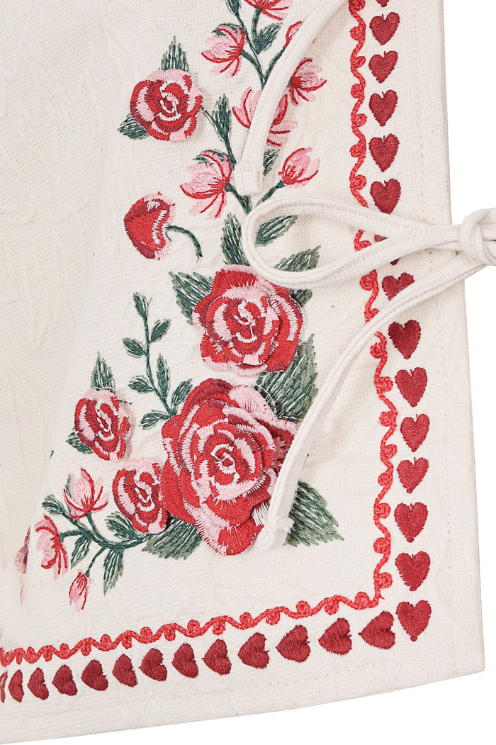 White cropped jacket with red and pink floral embroidery and heart trim along edges with tie-bow closure