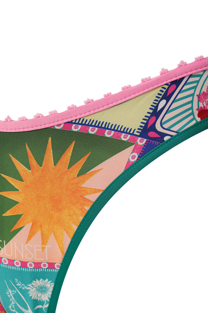 Avy bikini bottom in teal with handmade pink crochet trim, orange sunburst print on green background, and multicolor geometric embroidered details