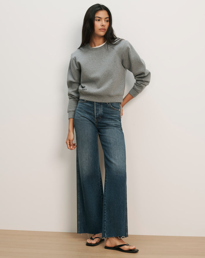 Veronica Beard Gray crewneck sweatshirt with raglan sleeves and dark wash wide-leg jeans with a raw hem.
