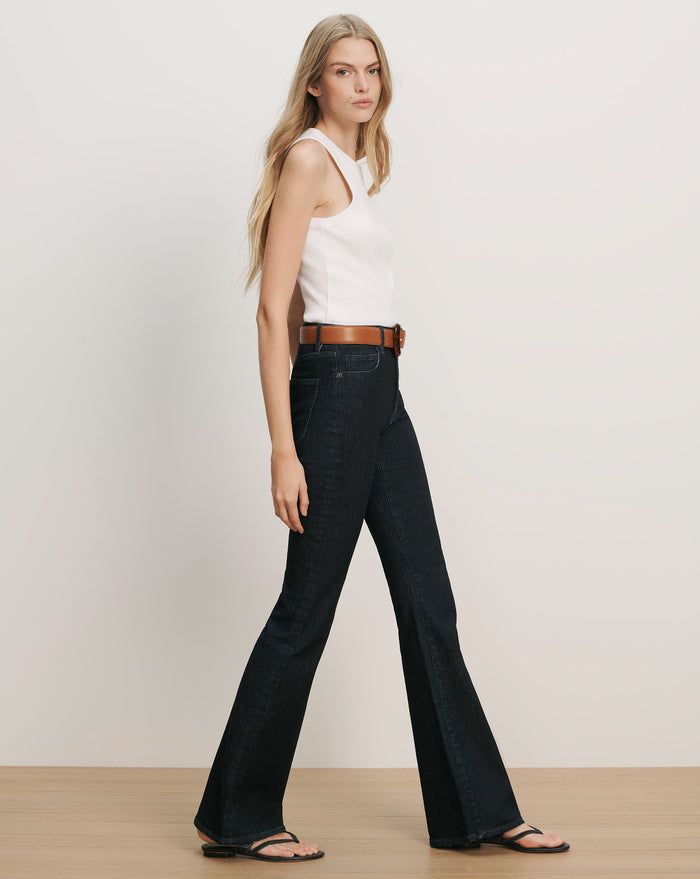 Veronica Beard White ribbed knit tank top with a high neck and dark wash flared jeans with a brown belt.
