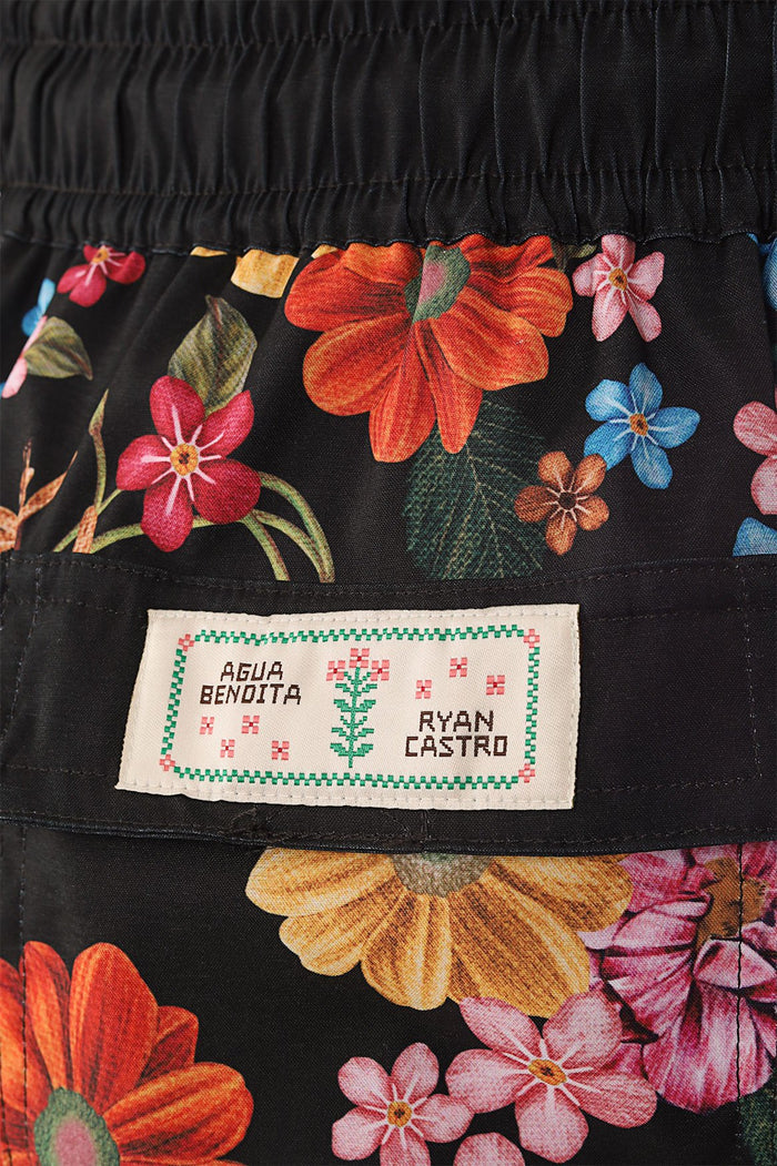 Black swim trunks with vibrant tropical floral print featuring orange, pink, blue, and yellow blooms with green foliage, elastic waistband detail