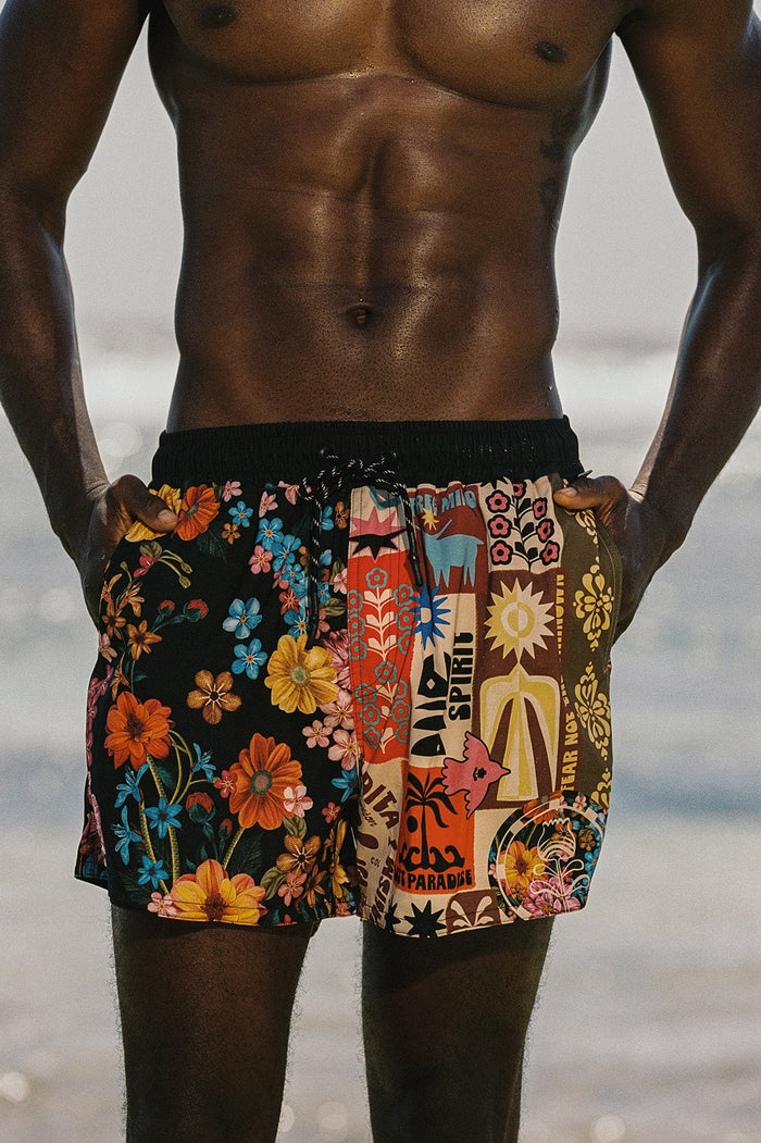 Men's swim trunks with mixed placement print featuring vertical panels of colorful florals and graphic elements on black elastic waistband