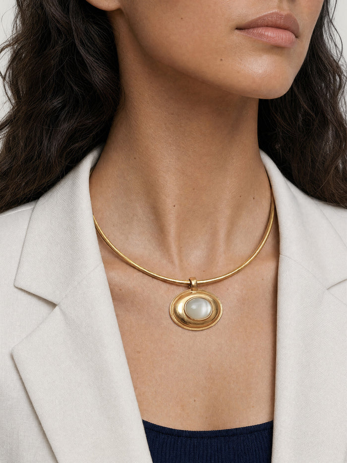 Veronica Beard White blazer, gold necklace with oval mother-of-pearl pendant.