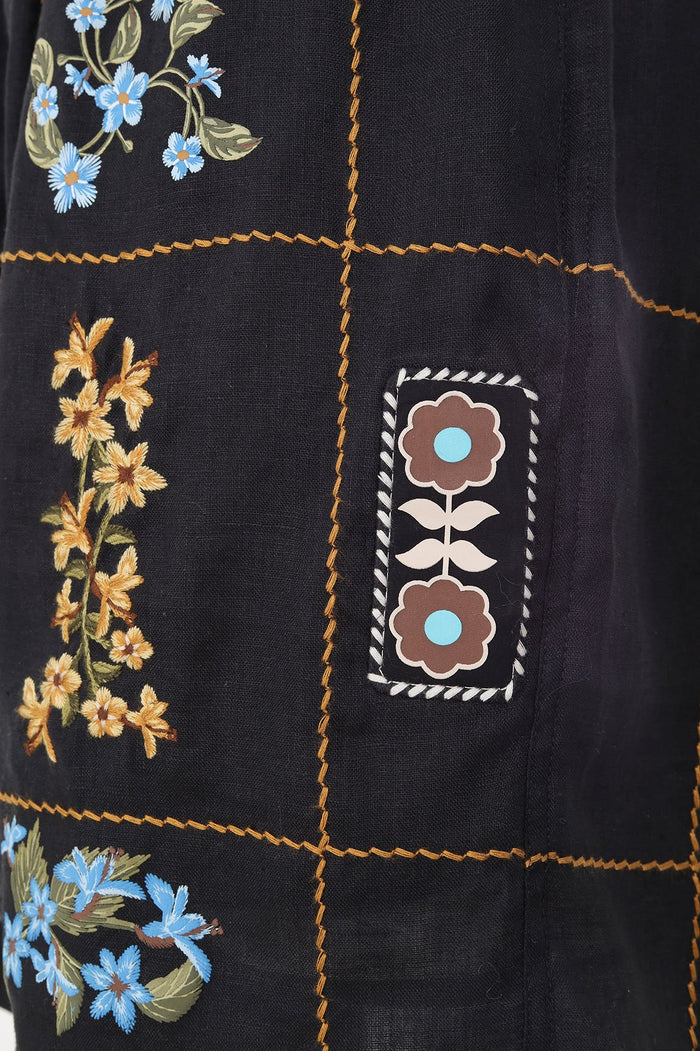 Black men's shorts with orange contrast stitching in grid pattern and embroidered floral patches featuring blue and yellow flowers