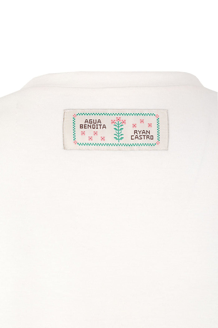 White cotton t-shirt with embroidered neck label featuring Agua Bendita and Ryan Castro branding in teal checkered border with pink pattern detail de…