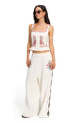 White Charlotte crop top with red floral embroidery, button front closure, ruffle hem, and matching wide-leg pants with embroidered side detail
