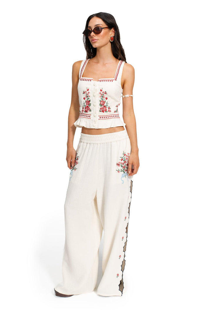 White Charlotte crop top with red floral embroidery, button front closure, ruffle hem, and matching wide-leg pants with embroidered side detail