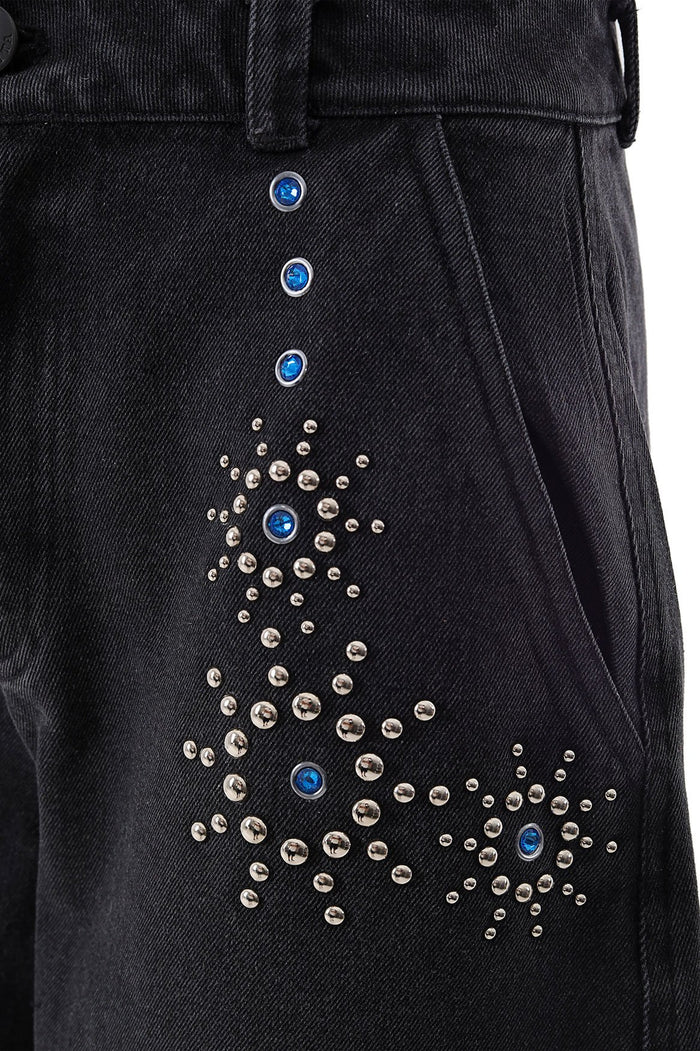 Black denim pants with blue rhinestone buttons and scattered silver stud embellishments along side seam
