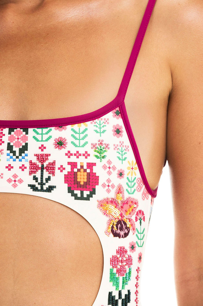 White one-piece swimsuit with magenta trim, featuring pixelated cross-stitch style pattern detail and geometric embroidered details with sequin embel…