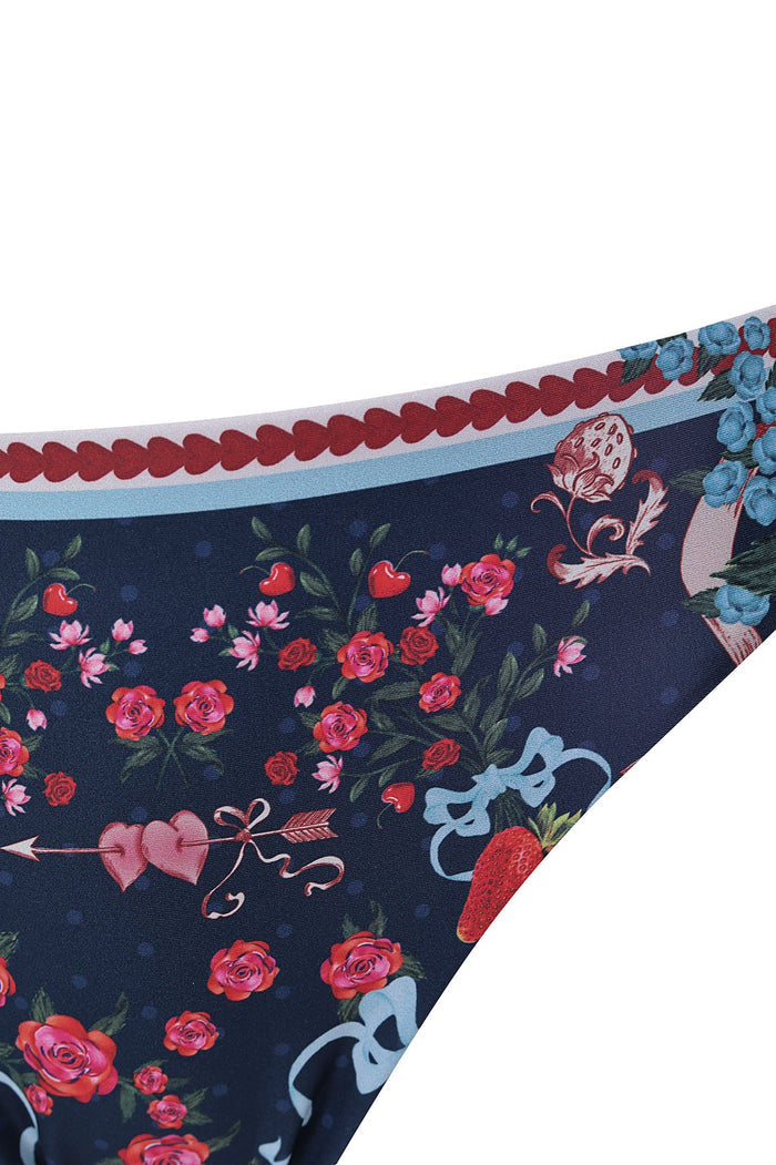 Navy bikini bottom with pattern detail print featuring roses, cherries, hearts, and strawberries, trimmed with scalloped red detailing and light blue…