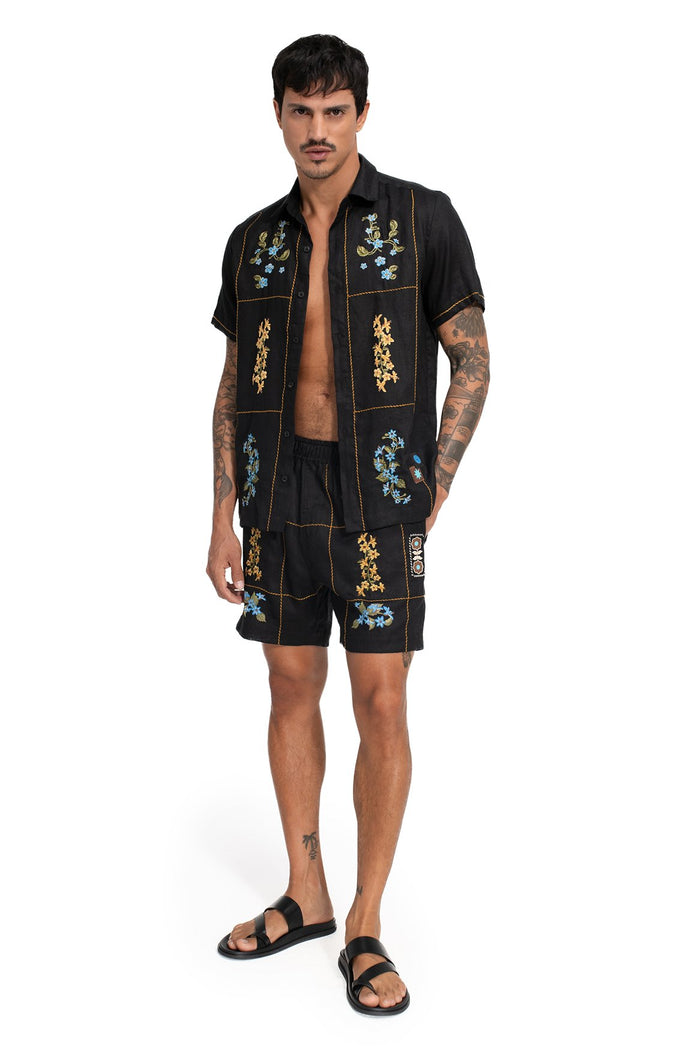 Black short-sleeve shirt with golden topstitching, grid-inspired panel layout, and embroidered floral details in blue and gold tones