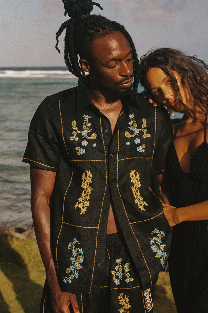 Black short-sleeve shirt with gold topstitching grid and embroidered blue and gold floral details on chest and lower panels
