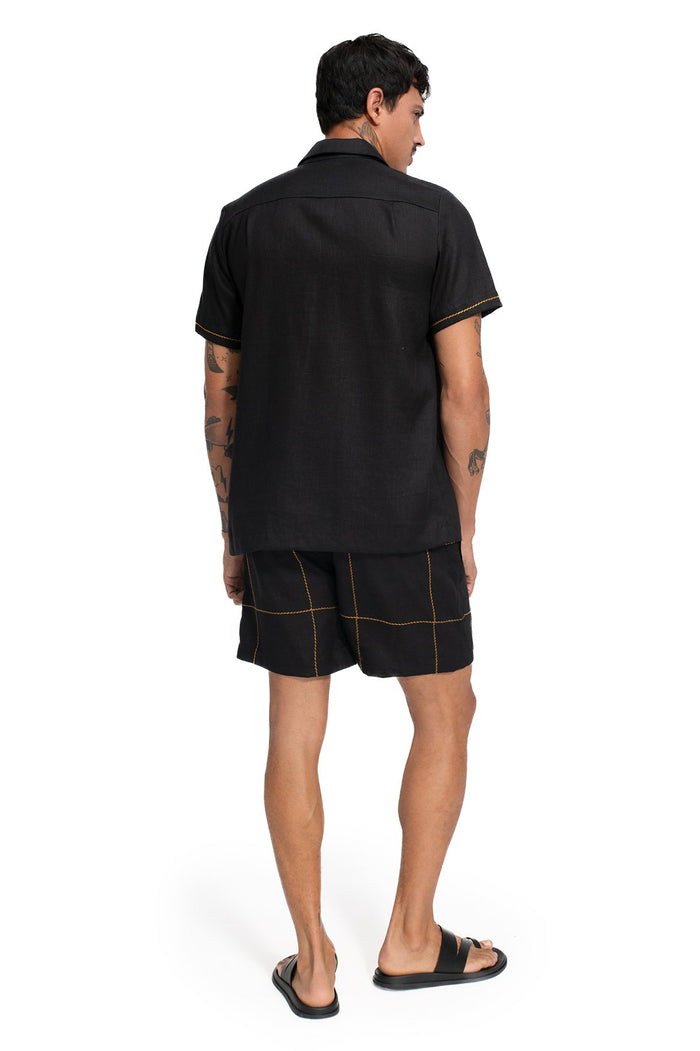 Black short-sleeve button-up shirt with contrast gold topstitching and matching shorts with grid pattern detail, back view