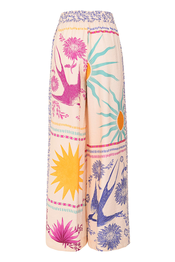 Wide-leg pants in peach with placement print featuring sunbursts, florals, and decorative border trim, back view
