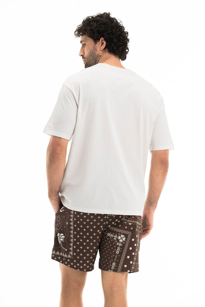 Jhoselyn t-shirt in white, back view, paired with brown swim shorts featuring bandana-inspired print with crosses and paisley details