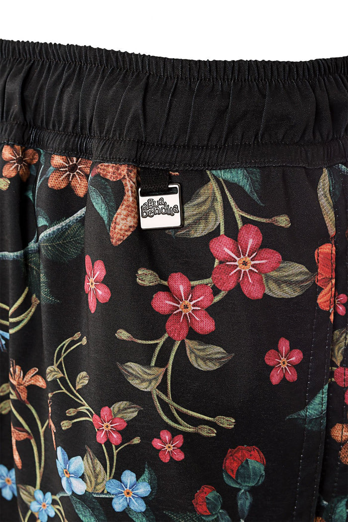 Black swim trunks with allover floral print in pink, coral, blue and green tones, showing elastic waistband and brand emblem