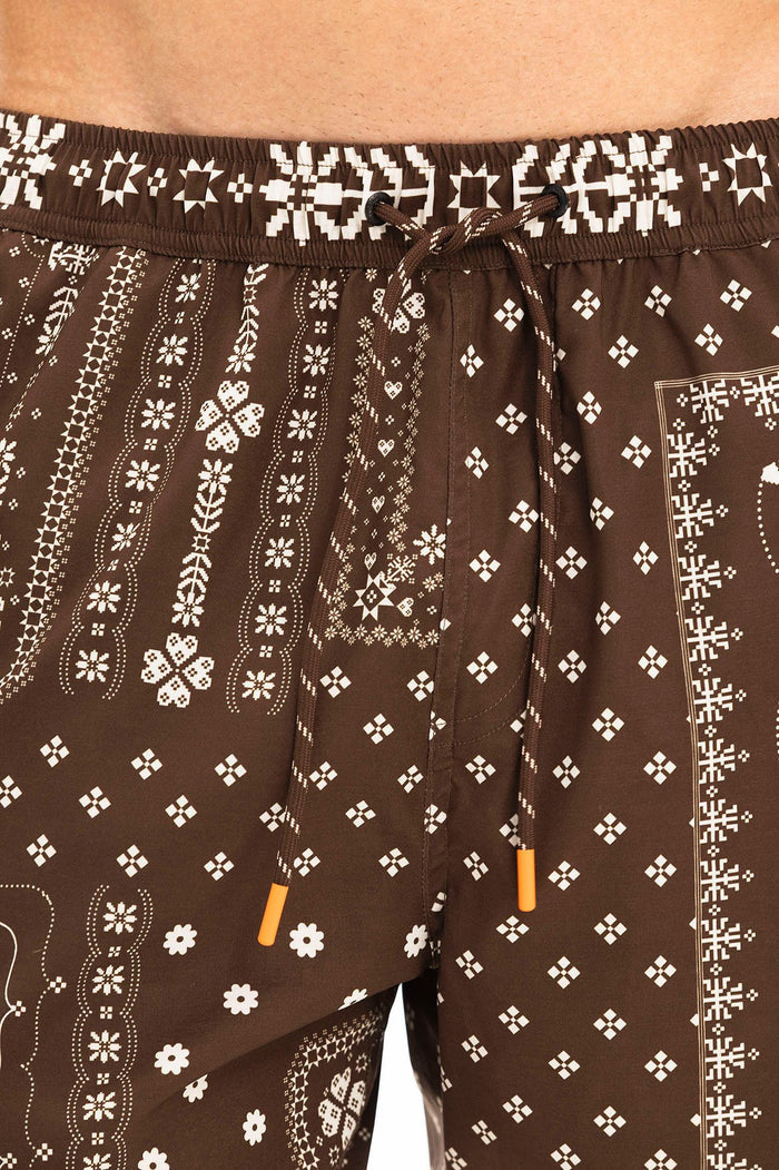 Brown swim trunks with white geometric patterns including diamond shapes, pattern detail clusters, and vertical decorative bands, featuring an elasti…