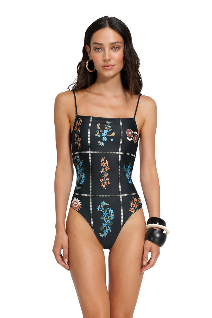 Black one-piece swimsuit with white contrast stitching in a grid pattern and colorful embroidered pattern detail details in blue, coral, and gold ton…