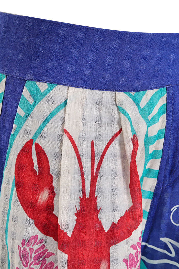 Lia shorts with blue waistband, pockets trimmed in blue, and multicolor placement print featuring red silhouettes, turquoise geometric patterns, and…