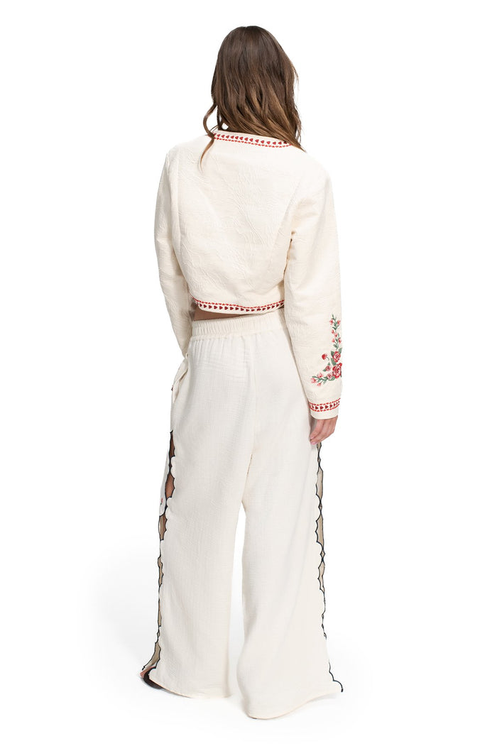 Lilia Pants in ivory with embroidered pattern detail details on sleeves, red trim at neckline and waist, and black scalloped laser-cut side seams, ba…