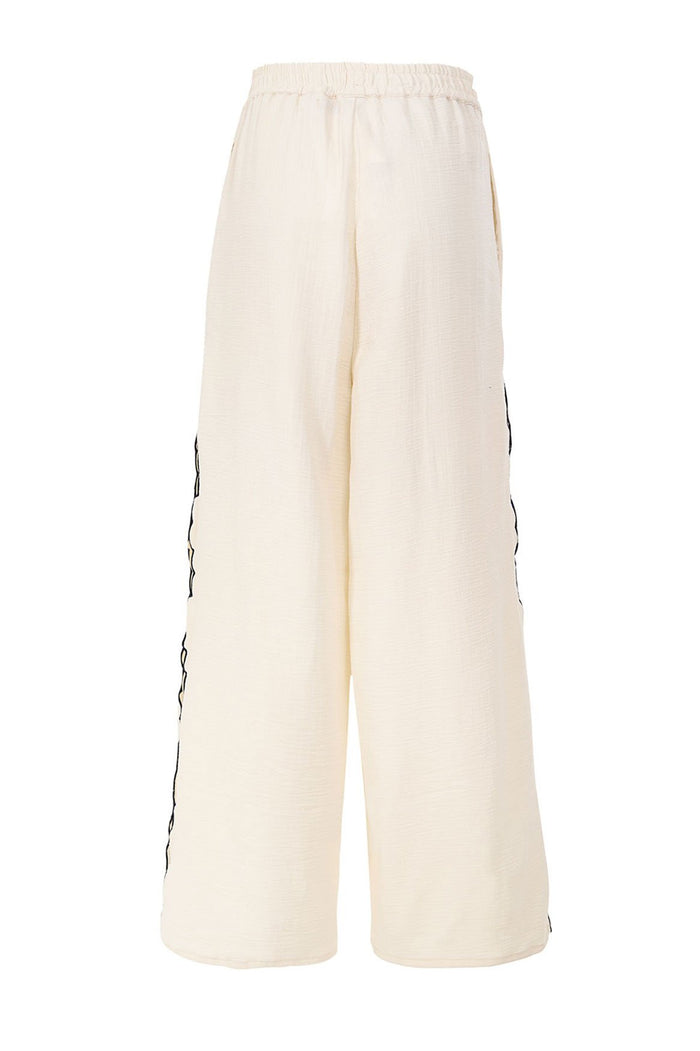 Cream wide-leg pants with elastic waist and black embroidered wave trim along side seams