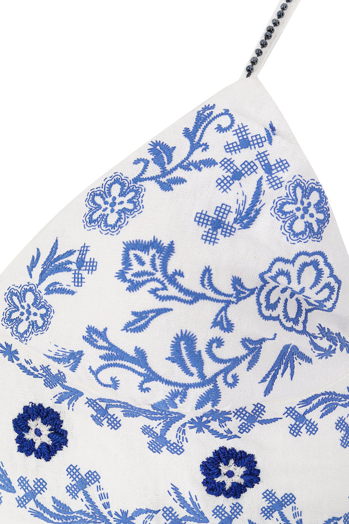 White crop top with blue embroidered pattern detail and scrollwork pattern, beaded strap detail