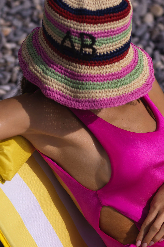 Handcrafted bucket hat with multicolor horizontal stripes in fuchsia, green, navy, red, and natural tones with embroidered letters on crown