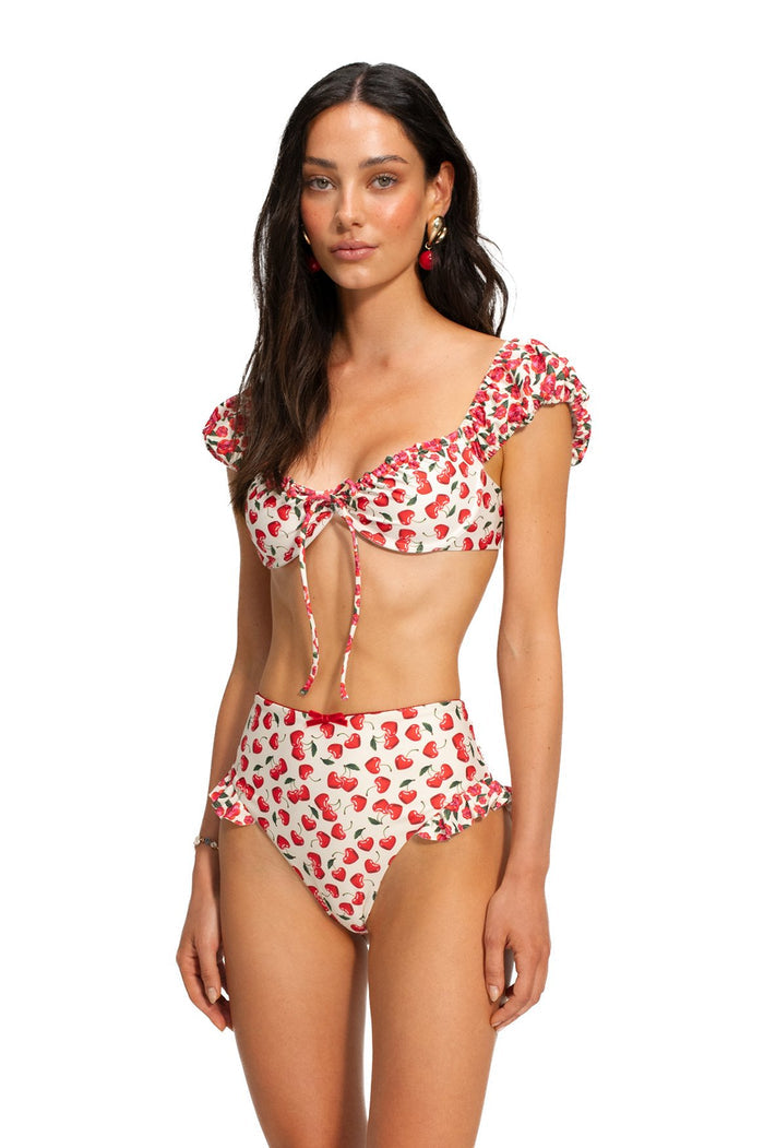 Lupita bikini top with ruffled cap sleeves and tie-front detail, cream base with red strawberry print, matching high-waisted bottoms with ruffle trim