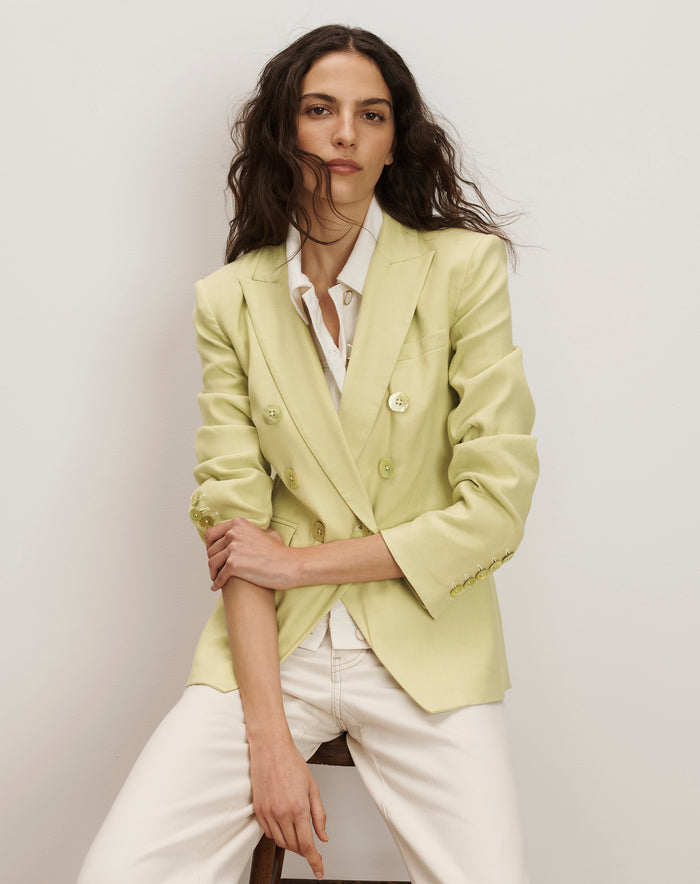 Veronica Beard Light green double-breasted blazer with peak lapels, paired with a white button-down shirt and off-white trousers.