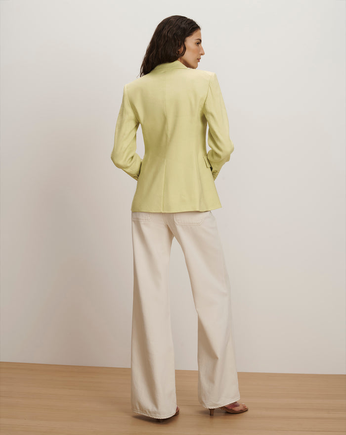 Veronica Beard A woman wears a light green blazer with a notched lapel and a single button closure, paired with wide-leg cream trousers.