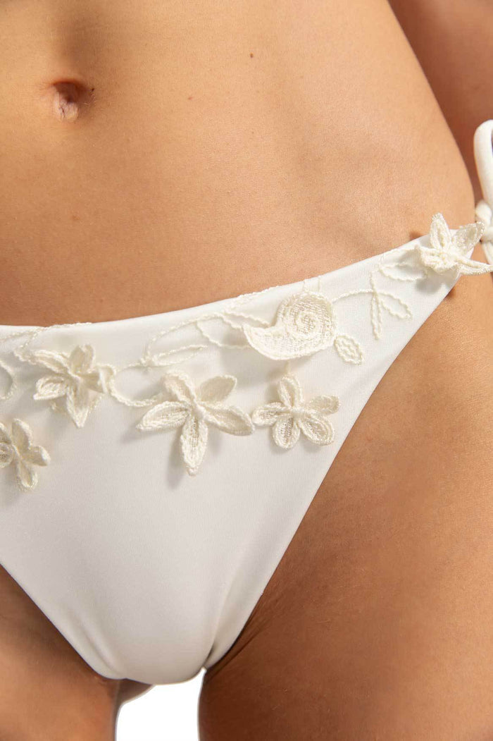 White bikini bottom with ruffled waistband and embroidered pattern detail appliqués along the trim