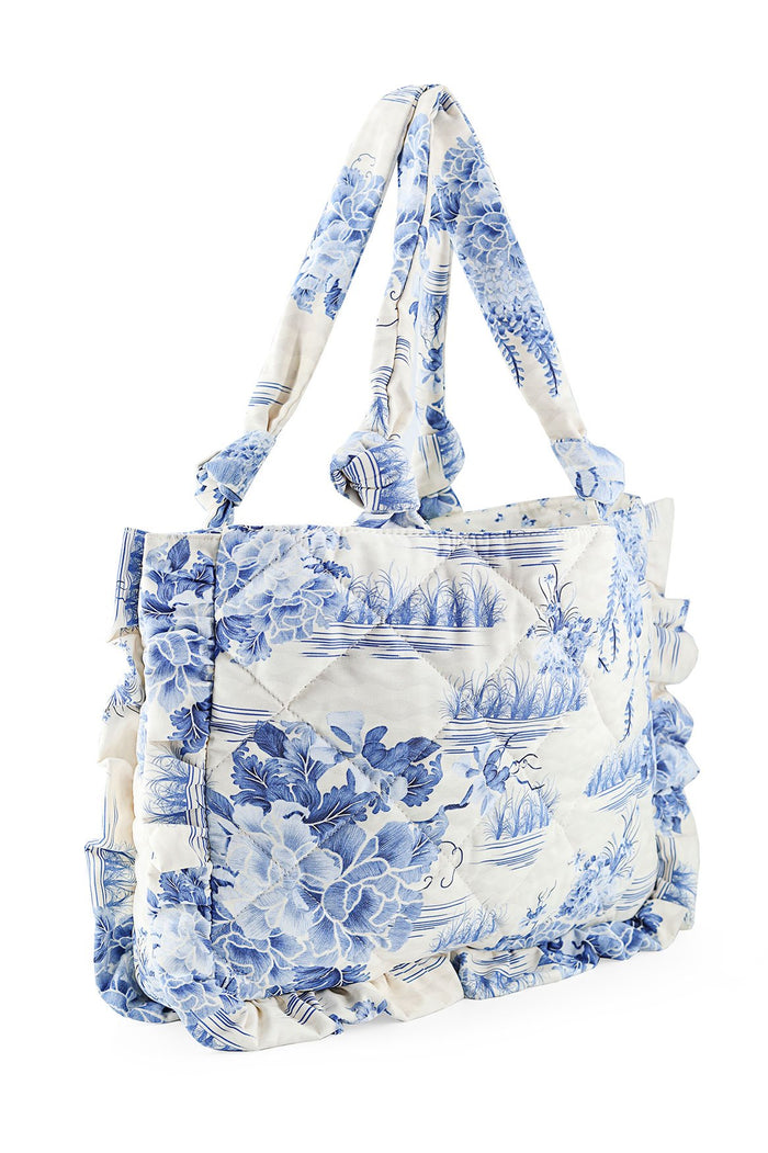 Nader Ambroise Bag in white with blue toile print featuring botanical and landscape scenery, quilted fabric with ruffle edges and knotted shoulder st…
