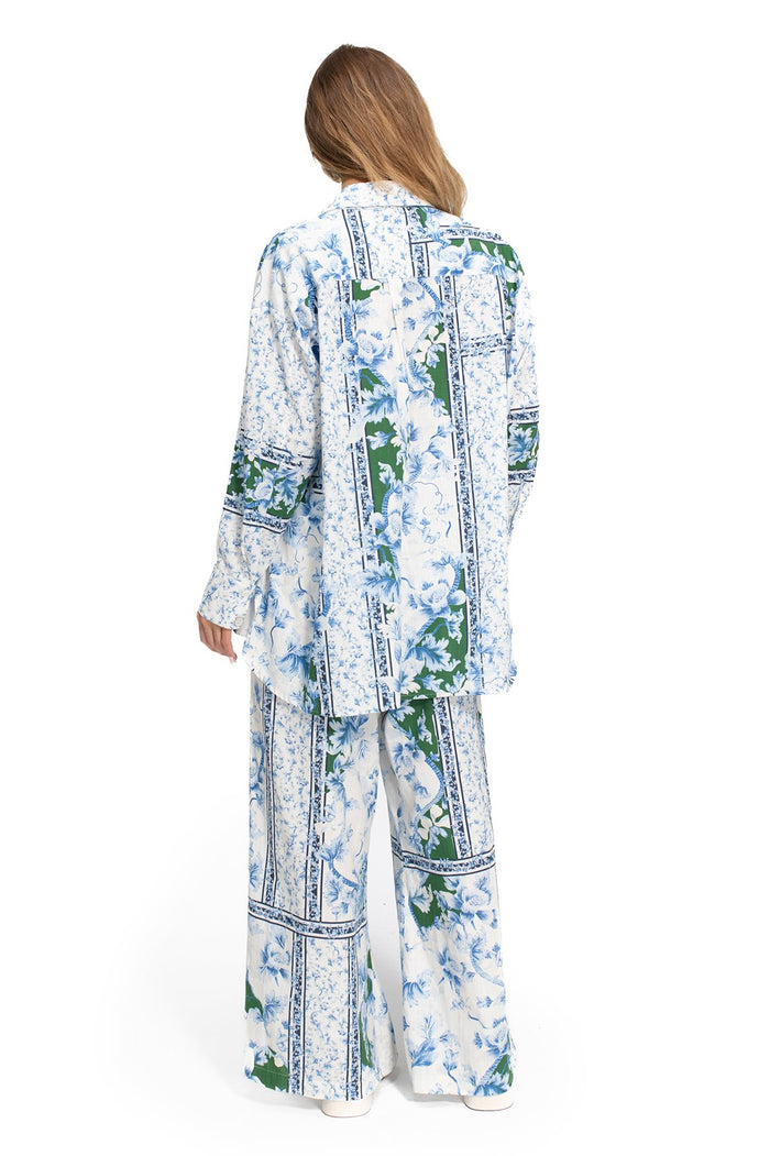 White long-sleeved button-up shirt with blue pattern detail print in vertical panels bordered by decorative trim and green leaf accents