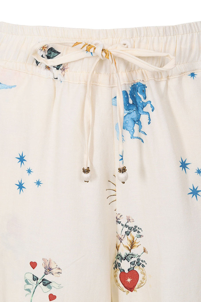 Cream drawstring pants with blue celestial print, red hearts, and pattern detail details