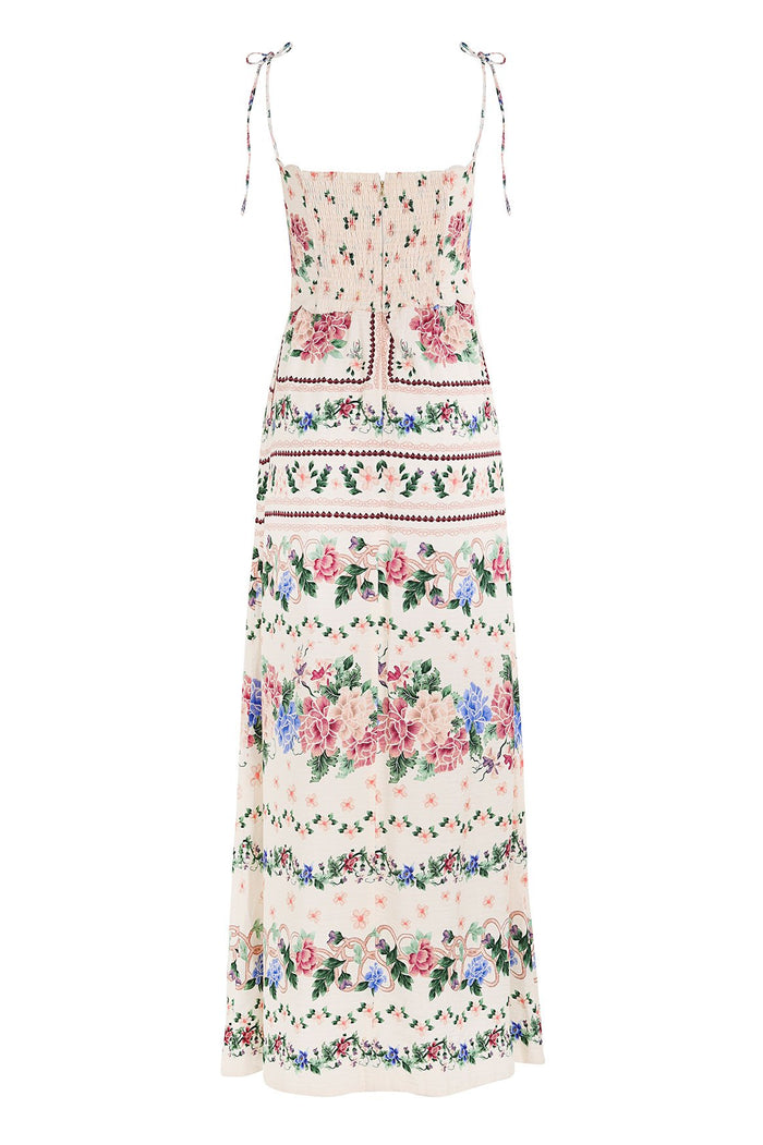 Cream maxi dress with smocked bodice, adjustable tie straps, and horizontal floral border print in pink, blue, and green