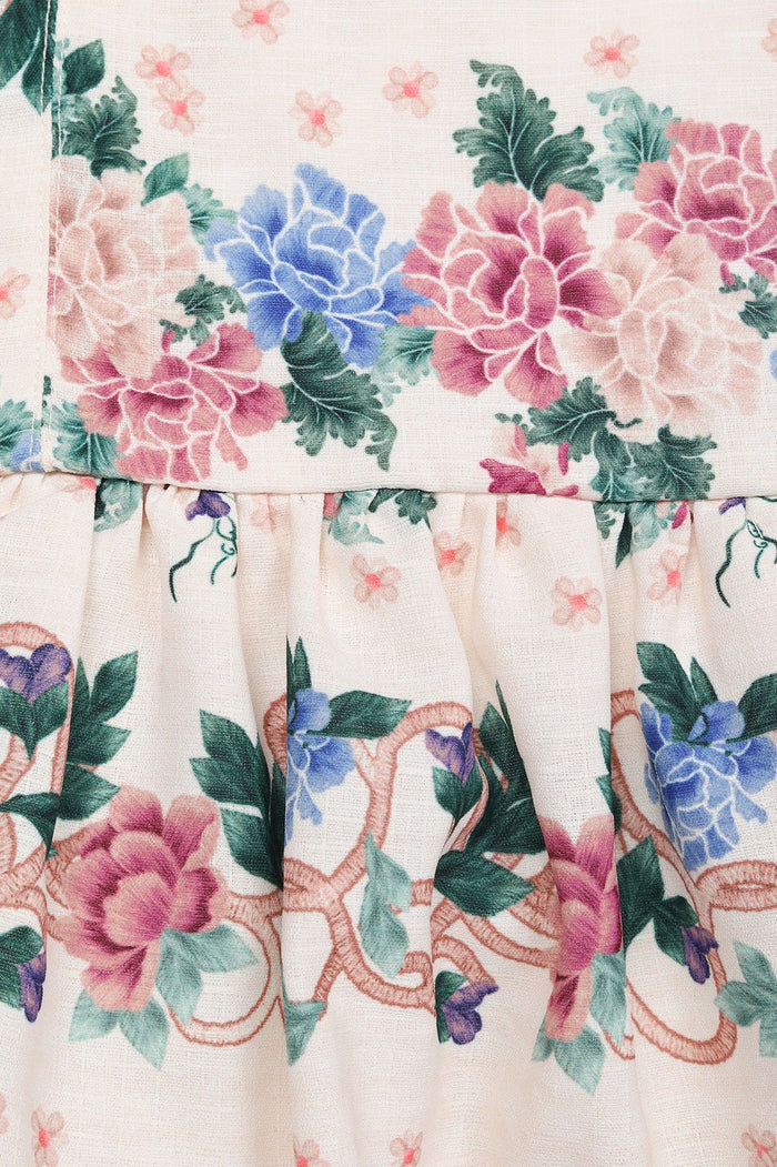 White dress with pink and blue floral print, contrast trim at neckline and hem, gathered skirt with decorative embroidered border