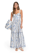 White maxi dress with blue pattern detail print arranged in vertical panels, structured bodice with adjustable straps, and tiered skirt