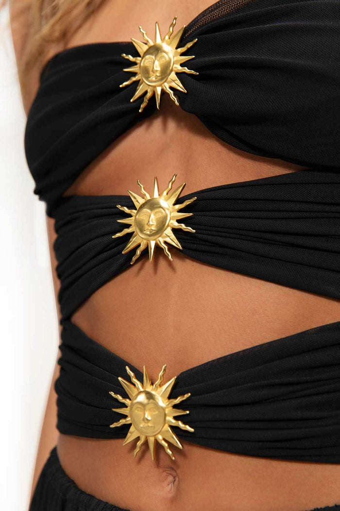 Black dress with ruched fabric bands and gold sun-face hardware appliqués at cutout details