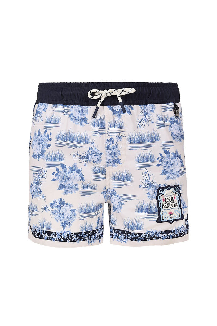 Kids' swim trunks with navy waistband, blue toile print of water scenes and botanical clusters on cream background, embroidered brand emblem at leg
