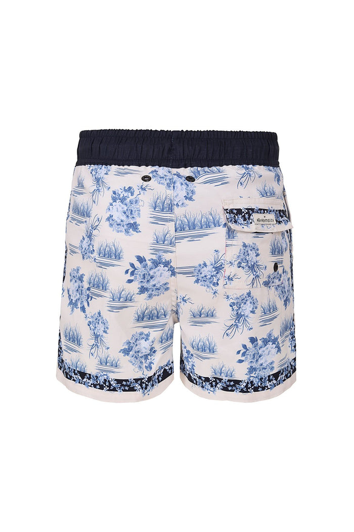 Kids' swim trunks in cream with blue pattern detail and botanical print, black elastic waistband, and contrasting patterned trim