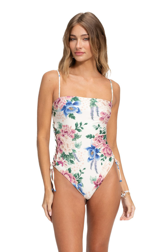 Nader Posh one-piece swimsuit with straight neckline, thin straps, and floral print in pink, blue, and green on white base with side lace-up ties