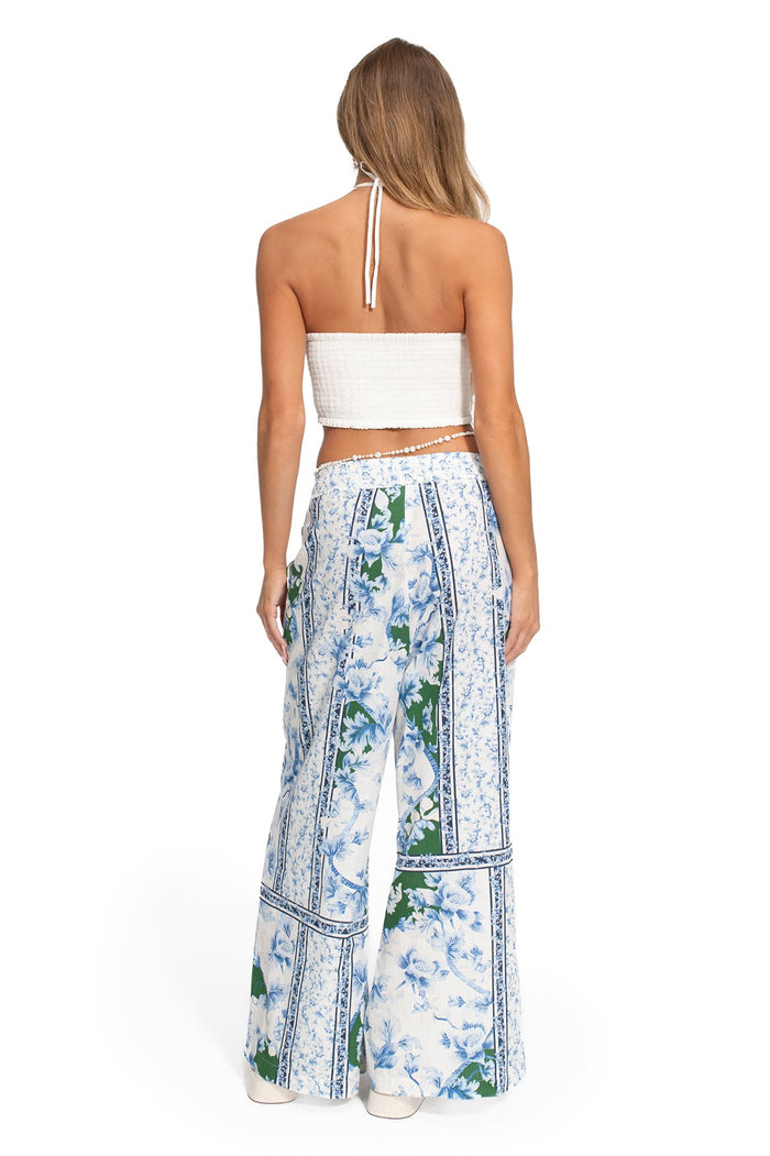 White smocked halter crop top with scalloped edges, paired with wide-leg pants featuring blue pattern detail print and green accents with bordered tr…