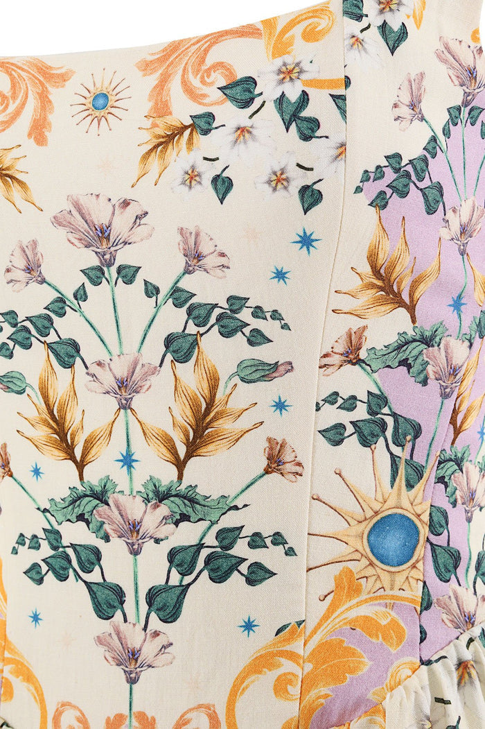 Cream mini dress with botanical print featuring purple flowers, golden leaves, blue stars, and sun illustrations across paneled fabric