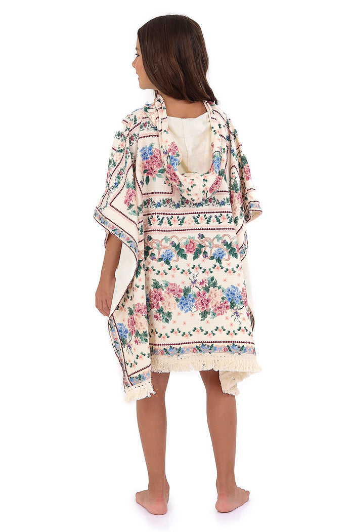 Hooded terry poncho towel in cream with pink and blue pattern detail print arranged in horizontal bands, dotted trim details, and fringe hem