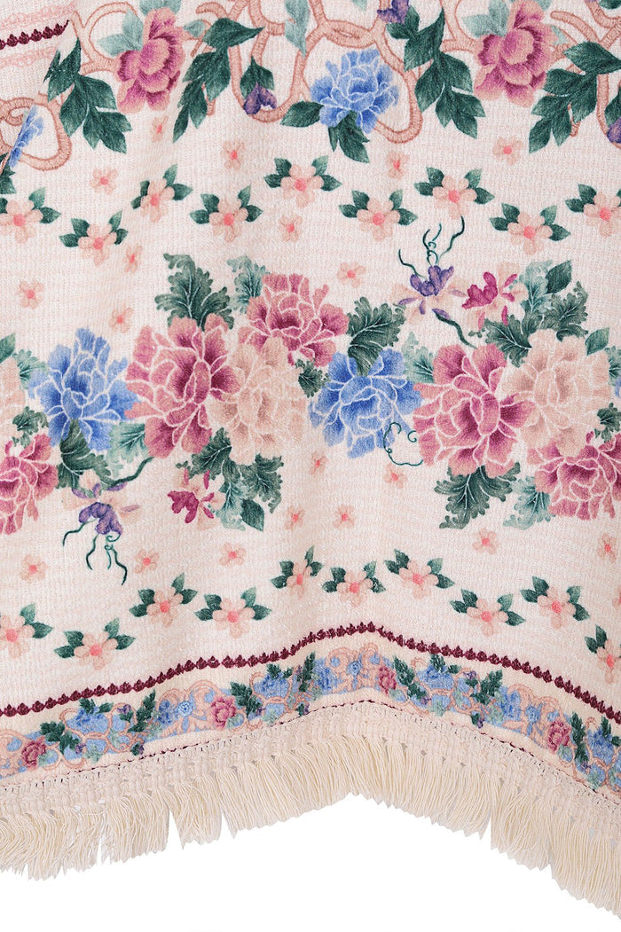 Blush pink terry poncho towel with pattern detail print featuring blue and pink blooms, green foliage, and cream fringe hem