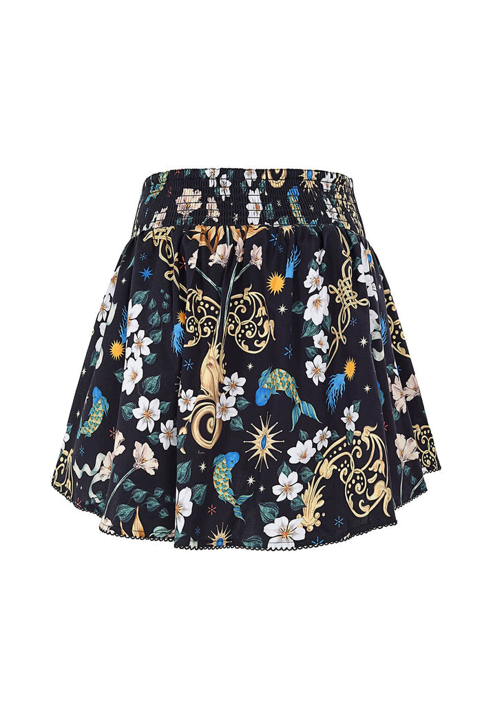 Black mini skirt with smocked elastic waistband, all-over print featuring white flowers, gold decorative scrollwork, blue stars, sun bursts, and gree…