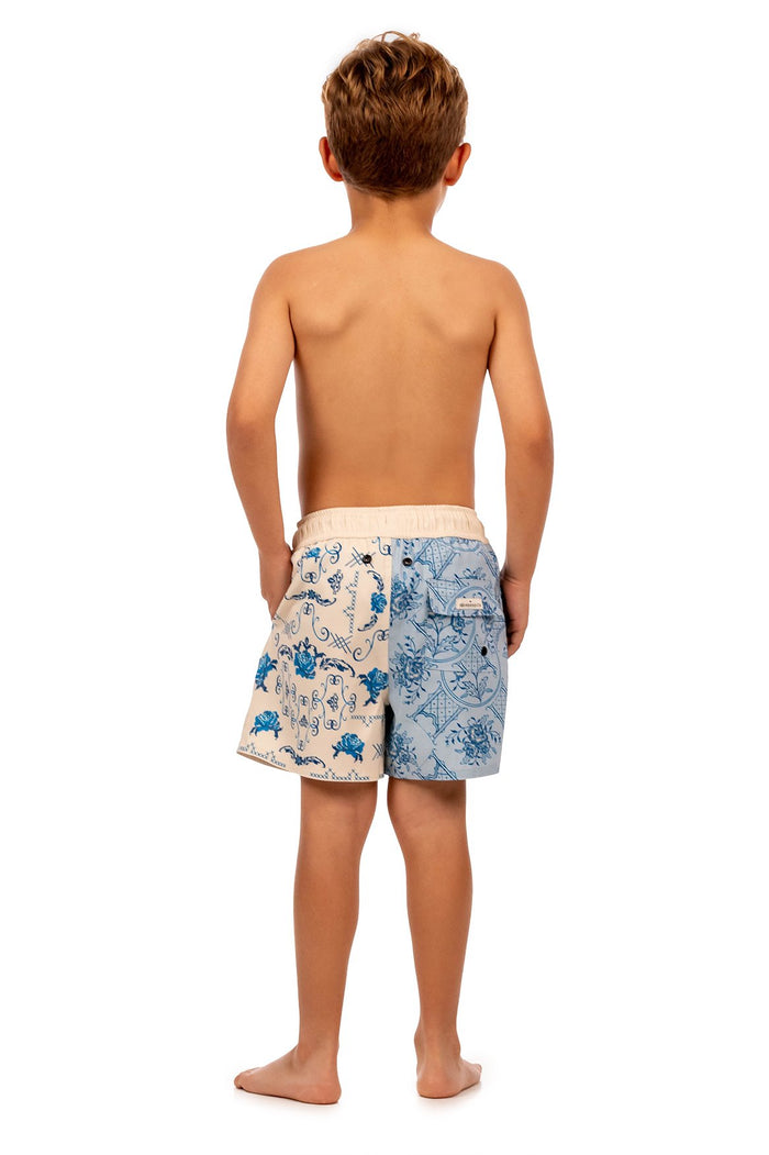 Boys' swim trunks with split-panel design: peach side with blue pattern detail scrollwork, light blue side with tile-inspired geometric pattern